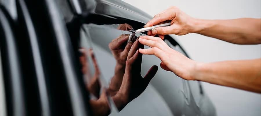 Hands applying window tint to a car, using a squeegee for smooth application.