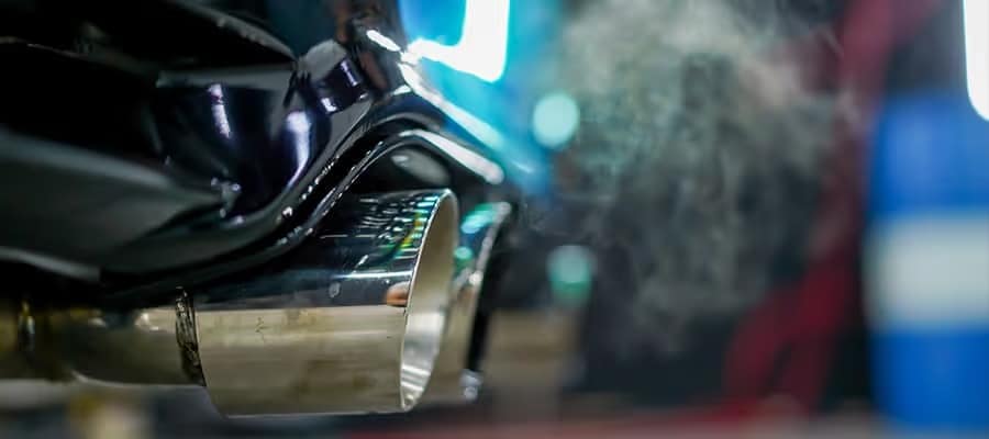 Car exhaust pipe emitting fumes in a garage setting, highlighting vehicle emissions.
