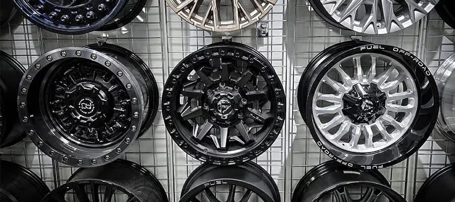Various styles of car rims displayed on a wire grid, featuring black and silver designs.