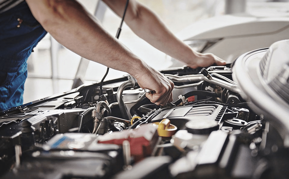 Mechanic working on car engine, checking components and ensuring proper maintenance in a garage.