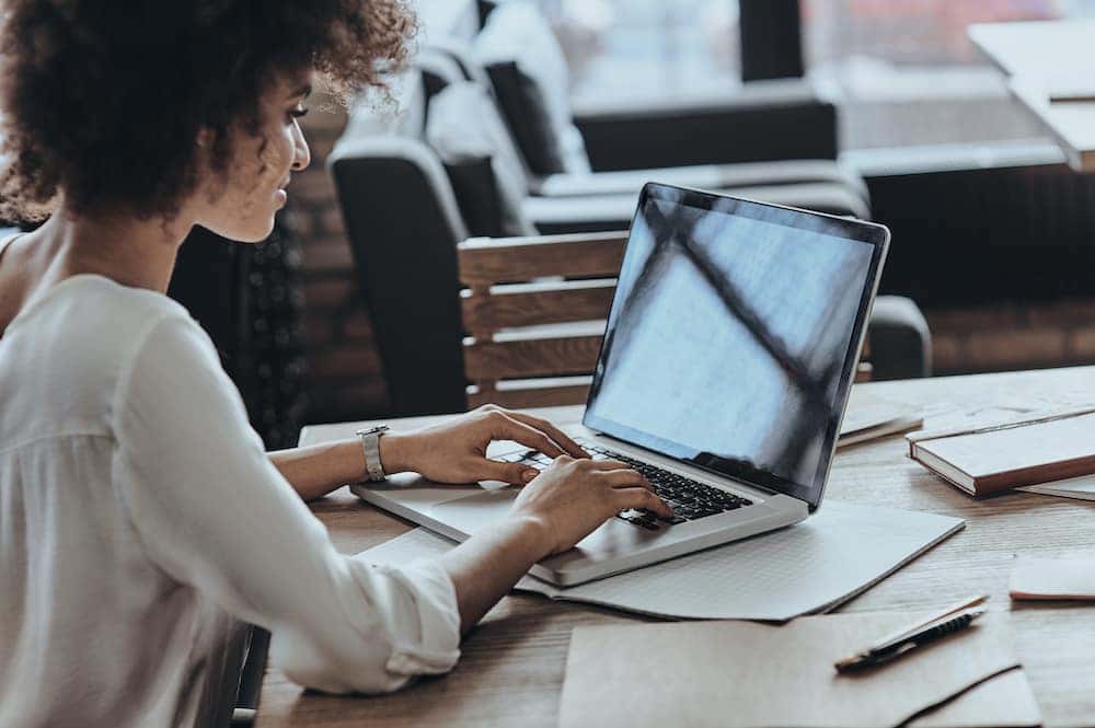 Person typing on a laptop at a wooden desk in a bright office setting.