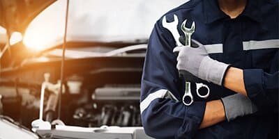 Mechanic with tools in front of a car engine at sunset, highlighting automotive repair services.