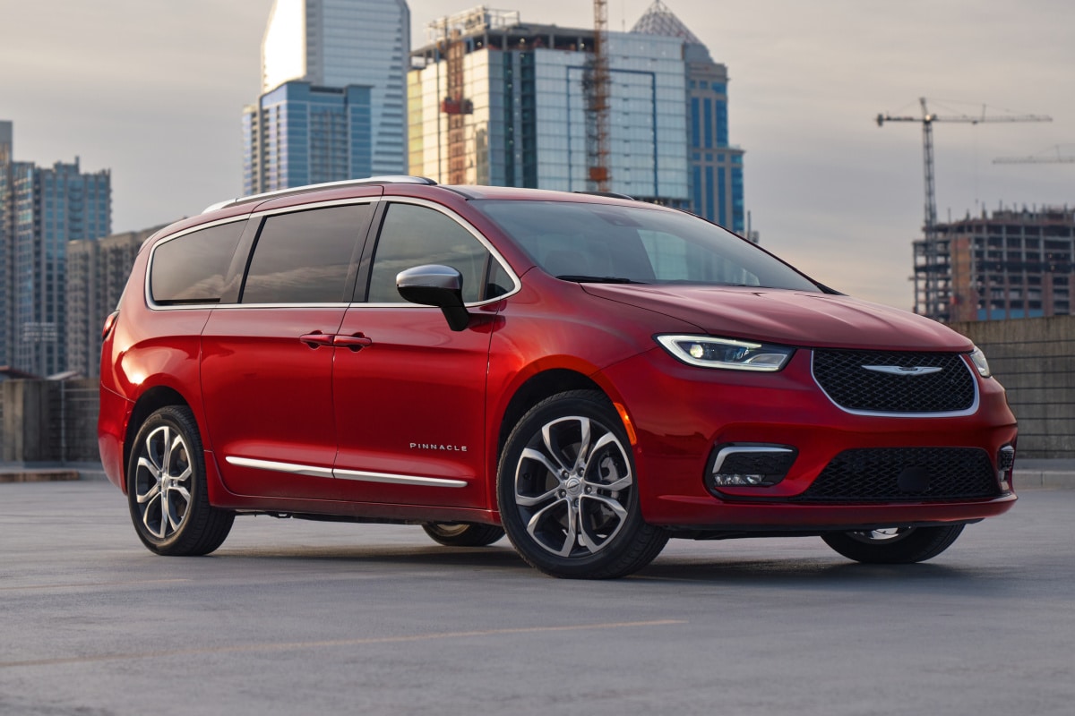 Red Chrysler minivan parked on a rooftop with city skyscrapers in the background.