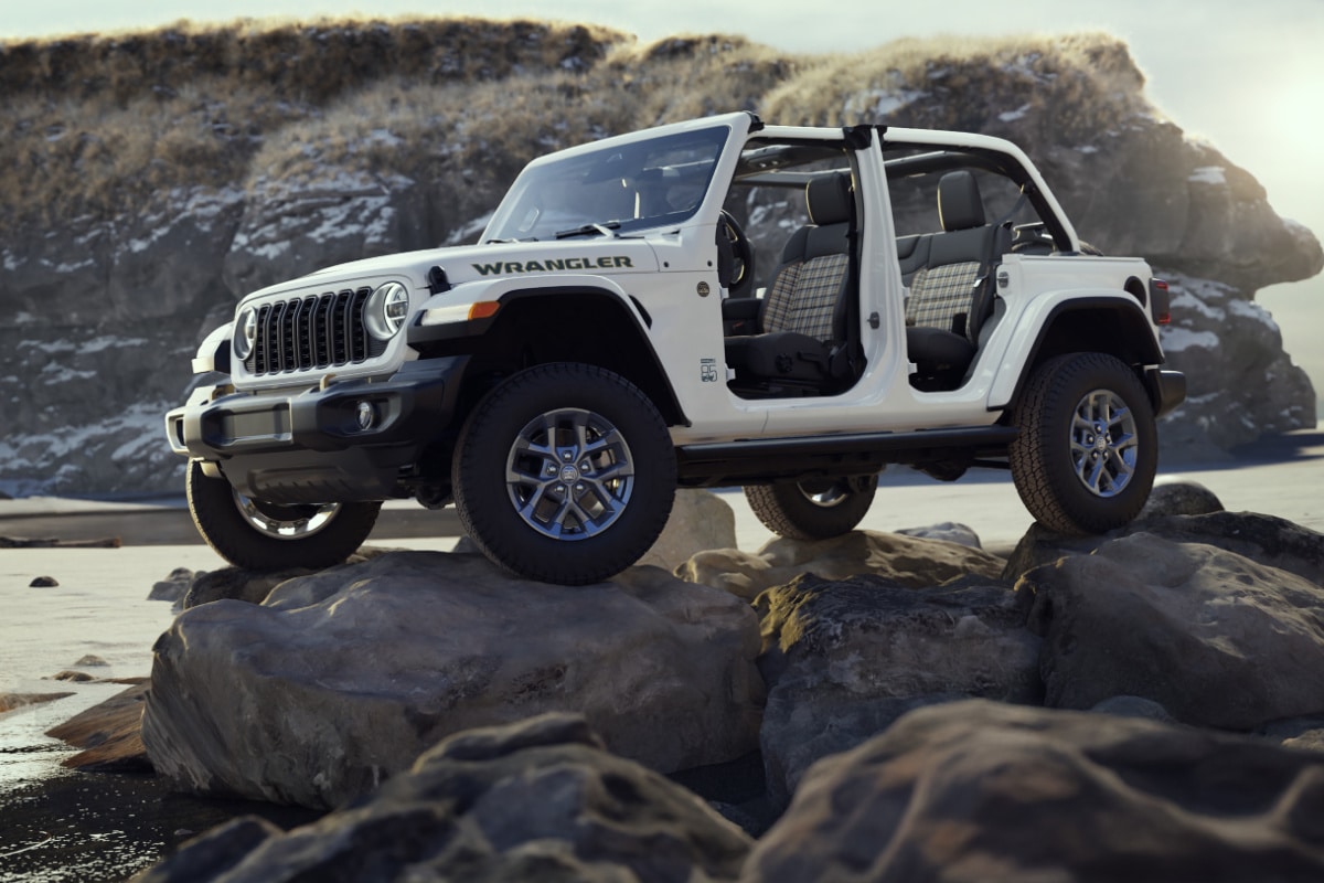 White Jeep Wrangler parked on rocky terrain by a scenic coastline, showcasing off-road capability.