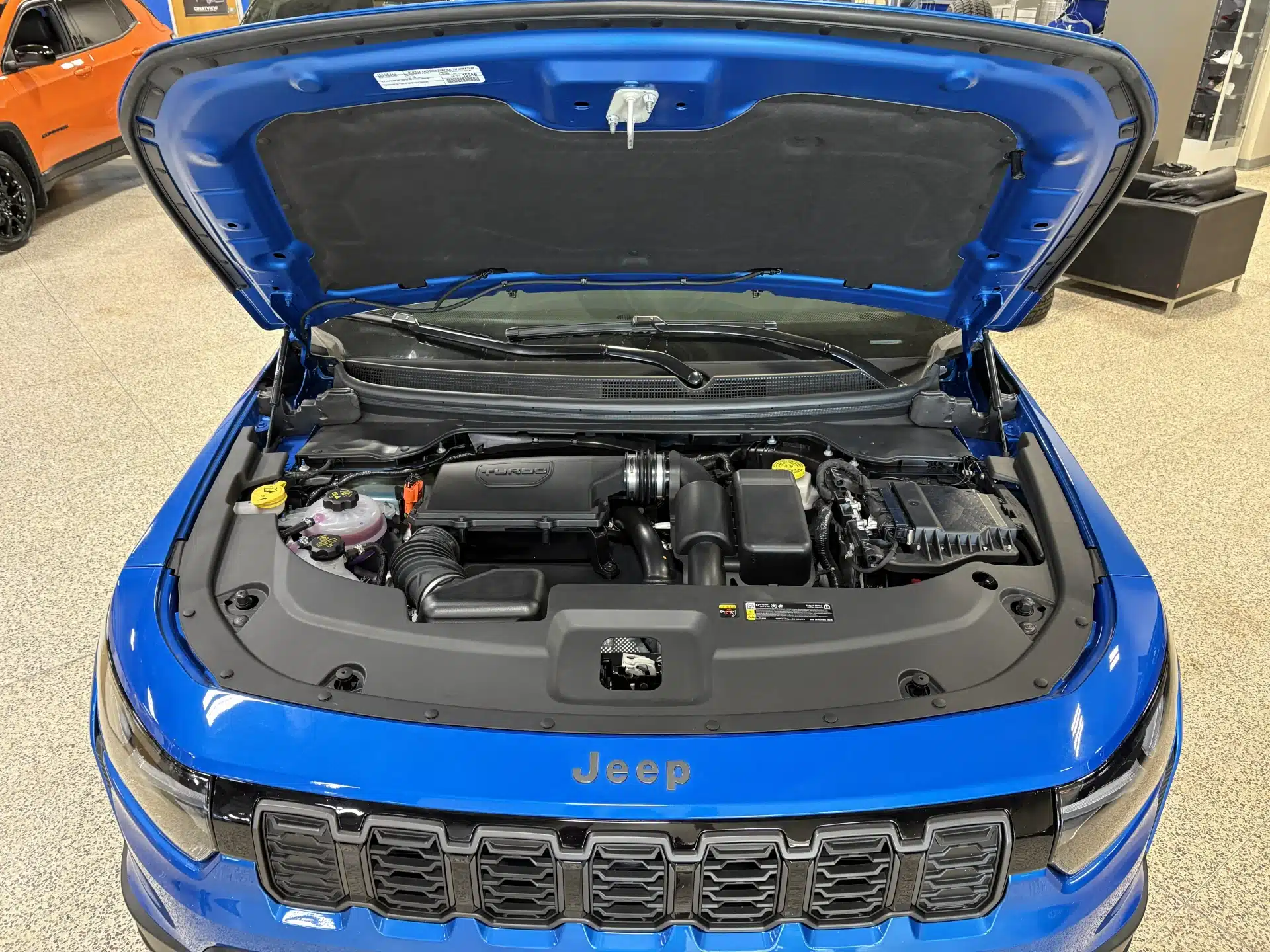 Blue Jeep with hood open, showcasing the engine and components in a showroom.