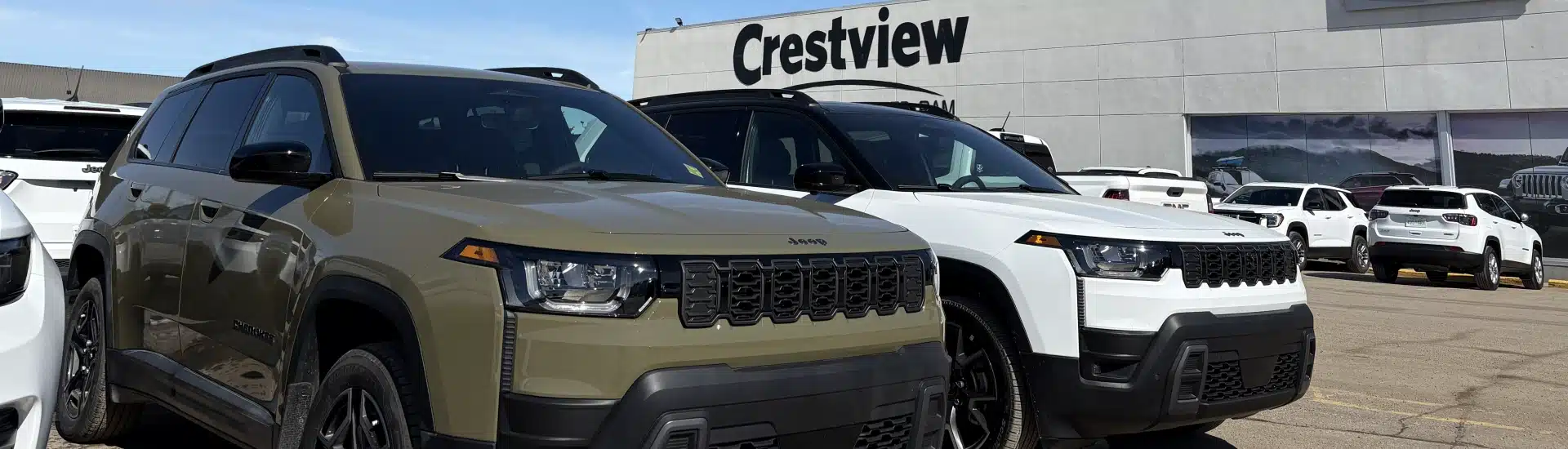 Two Jeep SUVs parked at a Crestview dealership under a clear sky.