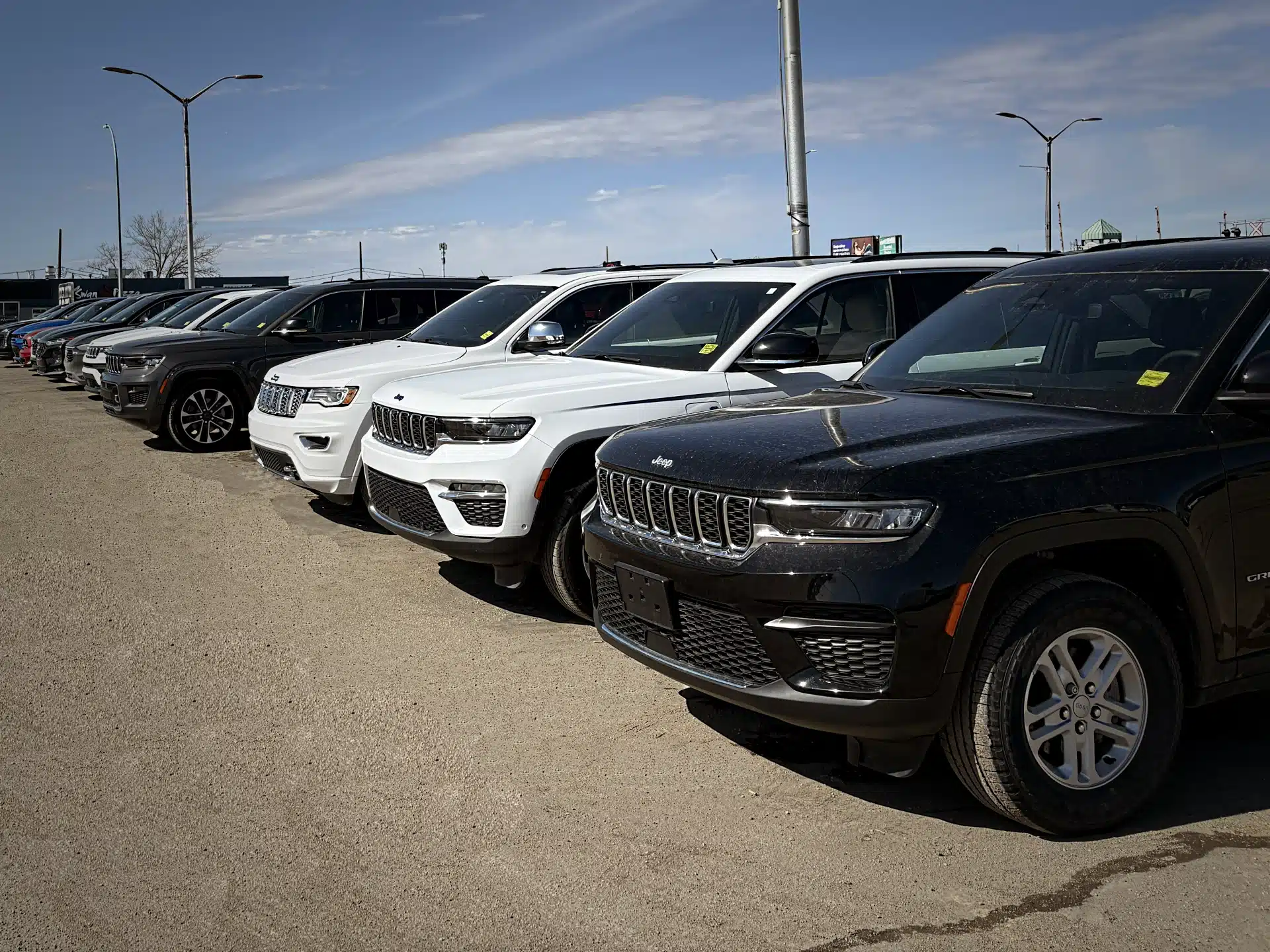 Line of parked SUVs in varying colors on a dealership lot under a clear blue sky.