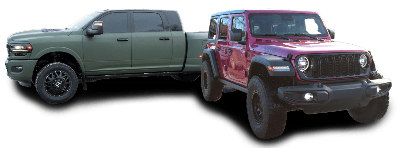 Two pick-up trucks, one red and one gray, are parked on a runway or a large parking lot. The red truck is at an angle that makes it look farther away and smaller, while the gray truck is closer and larger. Behind them, a city skyline with tall buildings can be seen under a blue sky with scattered cloud