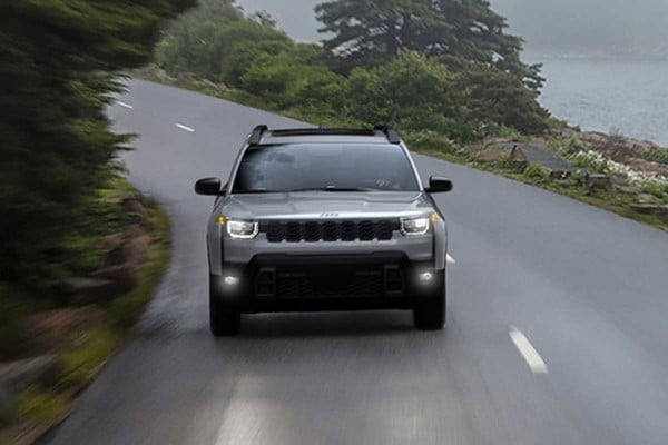SUV driving on a scenic coastal road, surrounded by lush greenery and mist.